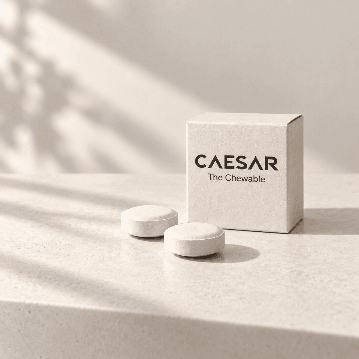 Two white tablets beside an ivory carton labeled Caesar The Chewable